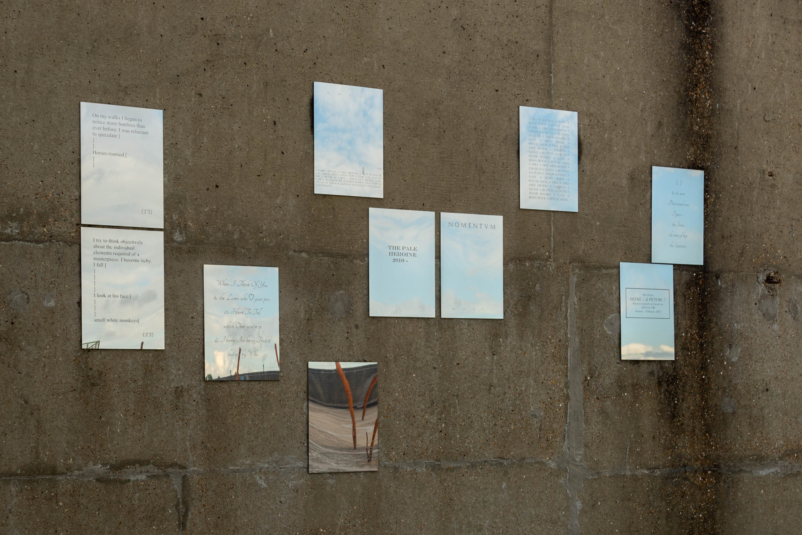 ID: a series of 10 mirror panels mounted on a concrete wall. They are each engraved with fragments of poetry in a variety of typefaces and formats.
